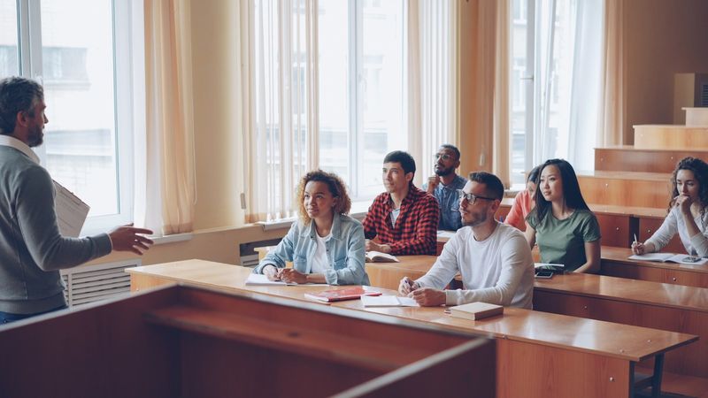 A lecturer addressing students seated at desks in a classroom